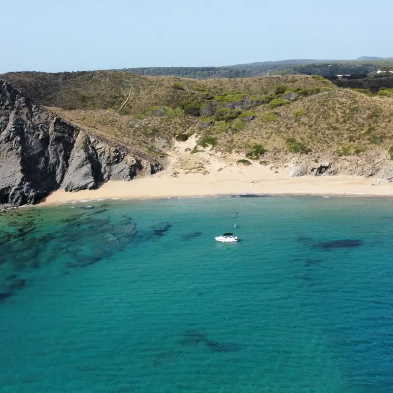 Barco con patrón en la costa norte de menorca en una playa desierta.